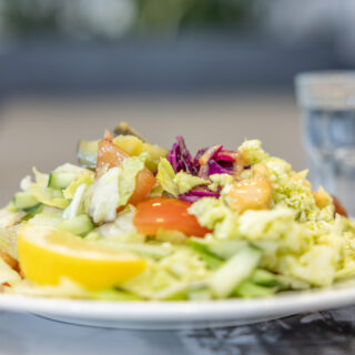 Lähikuva lautasesta joka on täynnä värikästä ruokaa muun muassa salaattia, tomaattia ja sitruunaa.