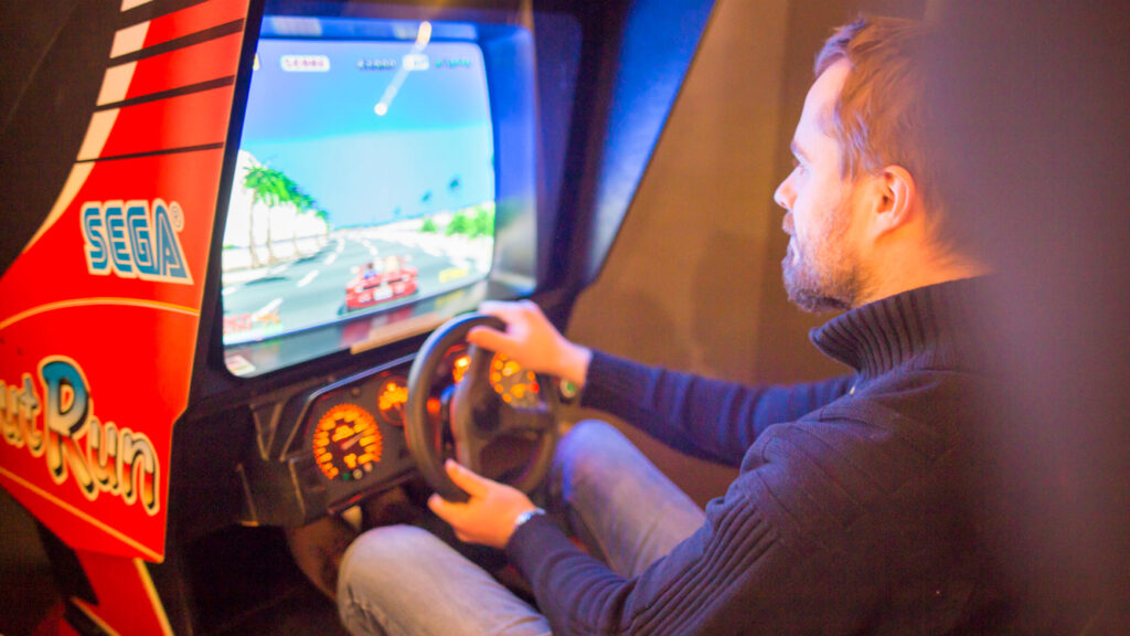 Mies pelaa videopeliä, jossa on ratti. Ruudulla näkyy ralliauto.