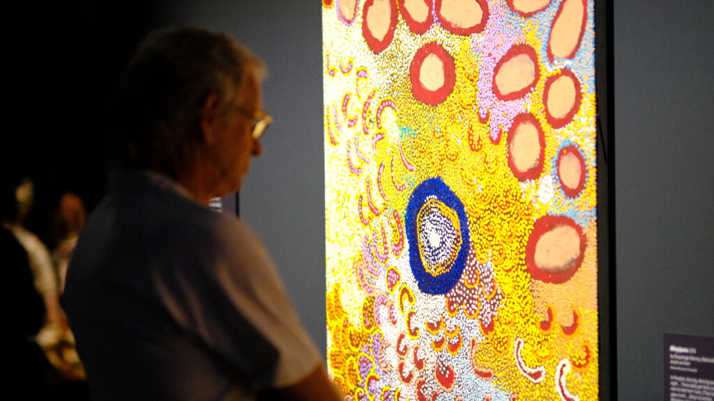 A man is looking at a colorful painting on the wall.