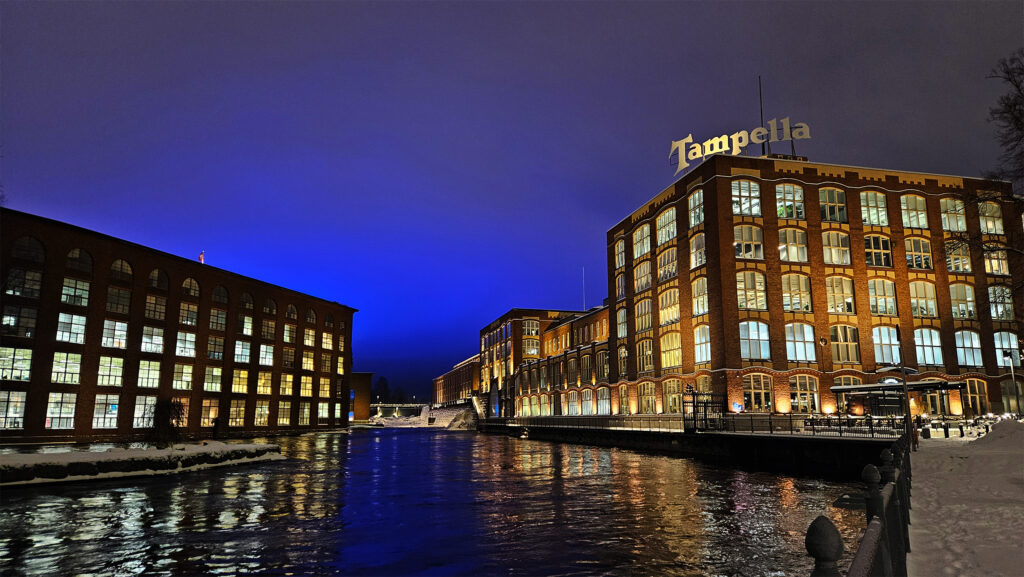 Maisemakuva Tammerkoskesta pimeänaikaan. Koskea reunustavat rakennukset, joiden ikkunoista loistaa valoa.