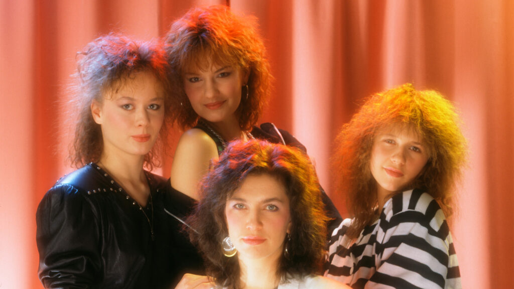 Neljä nuorta naista ryhmäkuvassa, 1980-luvun vaatteet ja kampaukset.