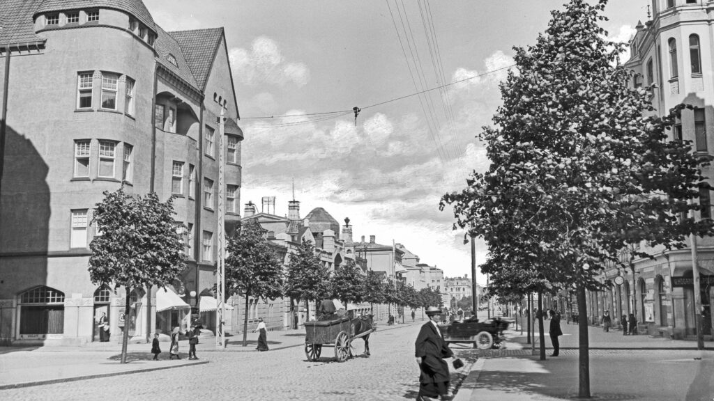 Mustavalkoisessa valokuvassa hämeenkatu 1900-luvun alkupuolella. Kuva otettu kesällä, puissa on lehdet. Kadulla kävelee ihmisiä ja hevosia.