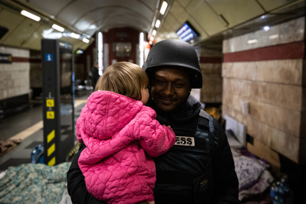 Pikkutyttö halaamassa luotiliiveihin pukeutunutta toimittajaa. Luotiliiveissä lukee PRESS.