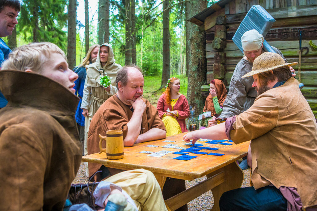 Erikoisiin asuihin pukeutuneita henkilöitä istuu pöydän ympärillä pelaamassa ulkona.