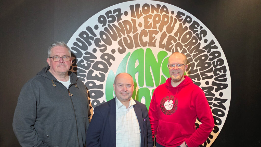 Kolme miestä kuvattu Manserock-kyltin edessä.