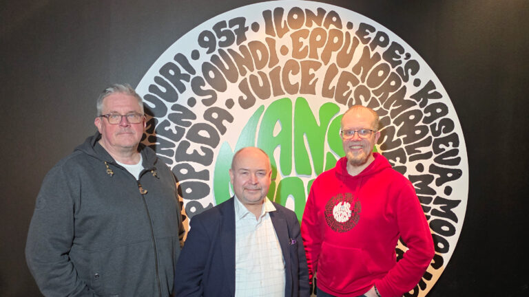 Kolme miestä kuvattu Manserock-kyltin edessä.