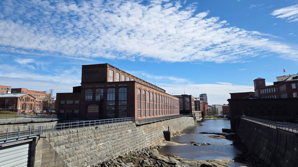 Vapriikin punatiilinen rakennus ulkoa kuvattuna. Rakennuksen reunassa alapuolella virtaa koski.